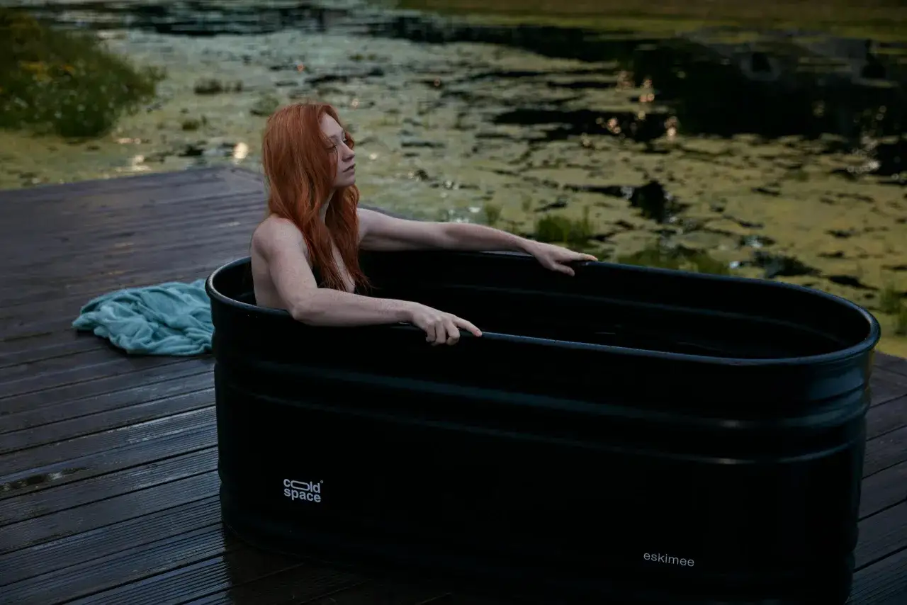 Ruda kobieta w wannie z zimną wodą, inspirowana metodą Wim Hof Polska. Relaks i hartowanie ciała nad jeziorem.
