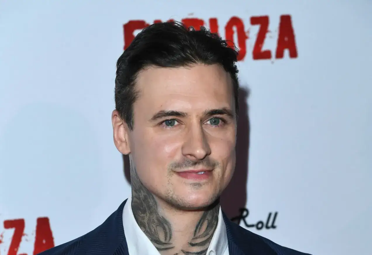 Aktor filmowy w Polsce, z tatuażami na szyi, na tle napisu 