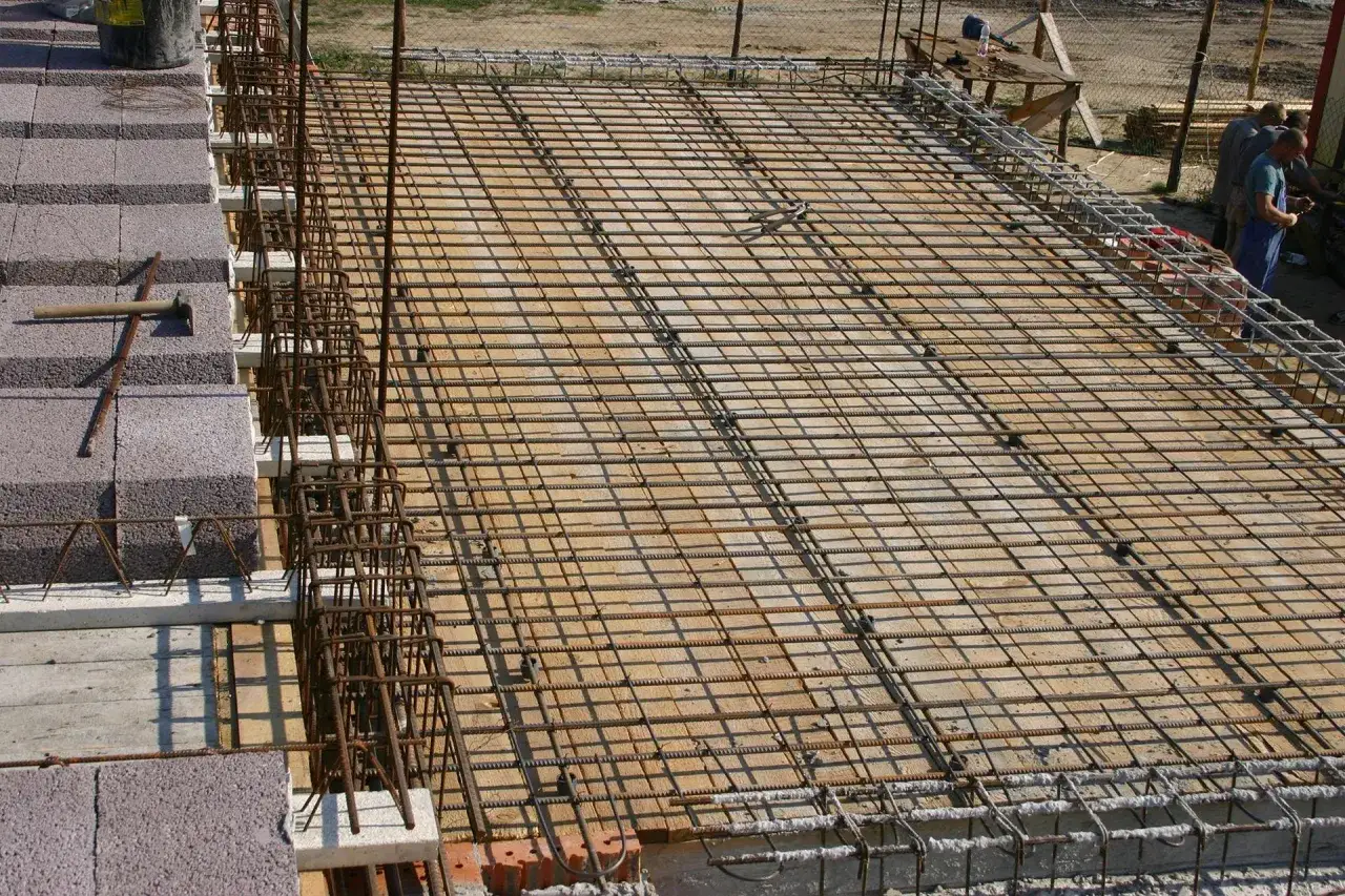 Siatka zbrojeniowa na stropie, przygotowana pod beton. Widać elementy konstrukcyjne i materiały budowlane.