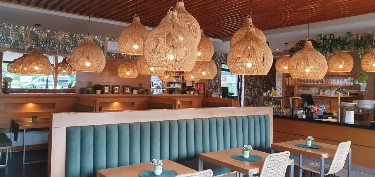 Przytulne wnętrze restauracji z wiklinowymi lampami, zielonymi kanapami i drewnianymi stołami. Idealne miejsce, gdzie na lunch w Piotrkowie.