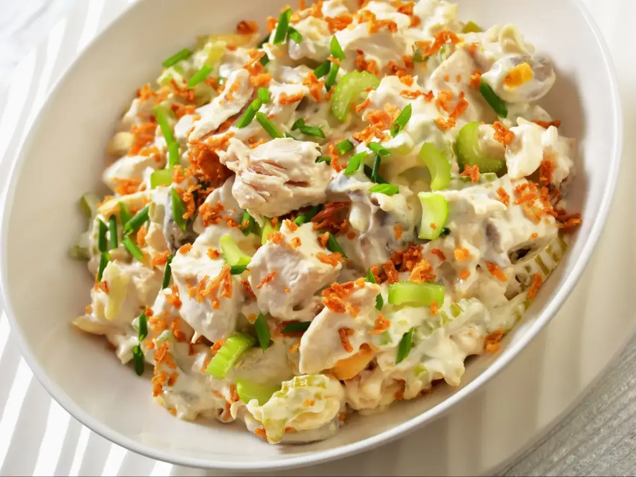 Pyszna pasta z gotowanego kurczaka z selerem, jajkiem i chrupiącą posypką, udekorowana szczypiorkiem.