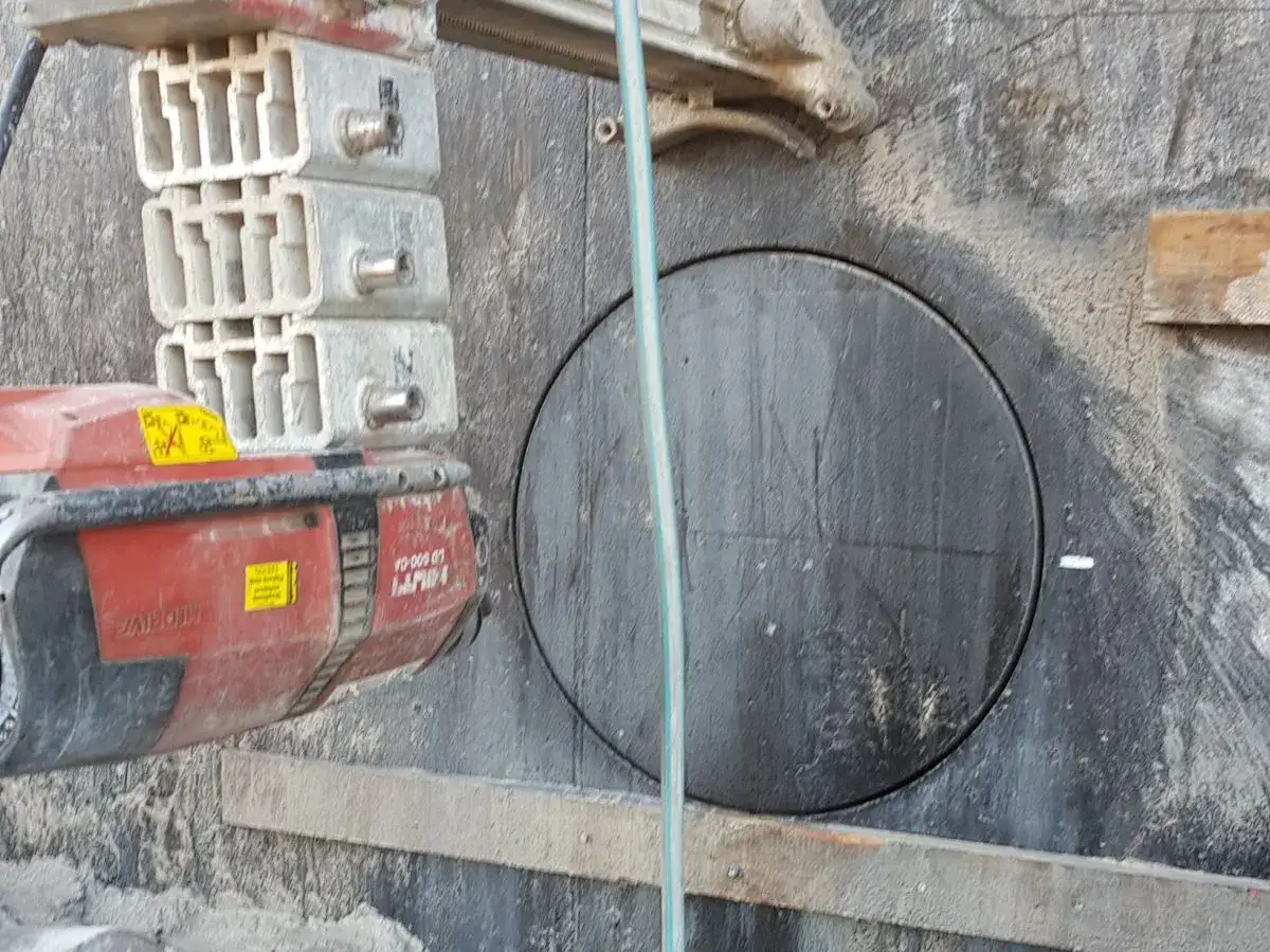 Widok na ścianę z wyciętym okręgiem, gdzie widać, jak idą kable w ścianie. Obok maszyna budowlana.