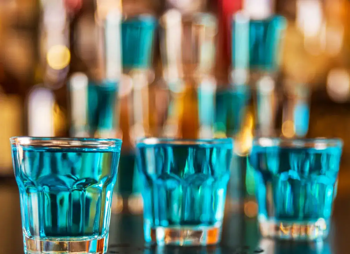 Błękitne shoty, jak w przepisie na Kamikadze, stoją w rzędach na barze.