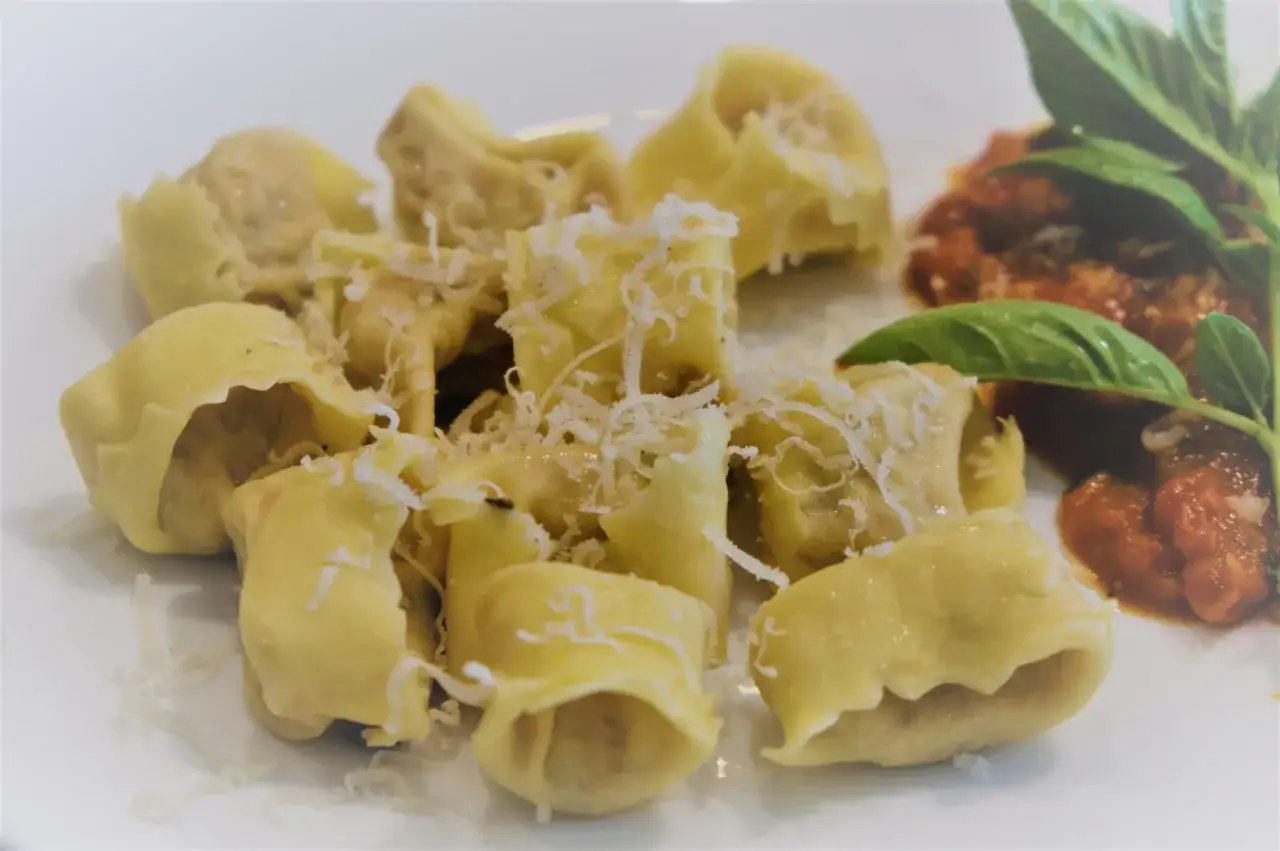 Pyszne tortellini posypane parmezanem, podane z sosem pomidorowym i listkami bazylii.