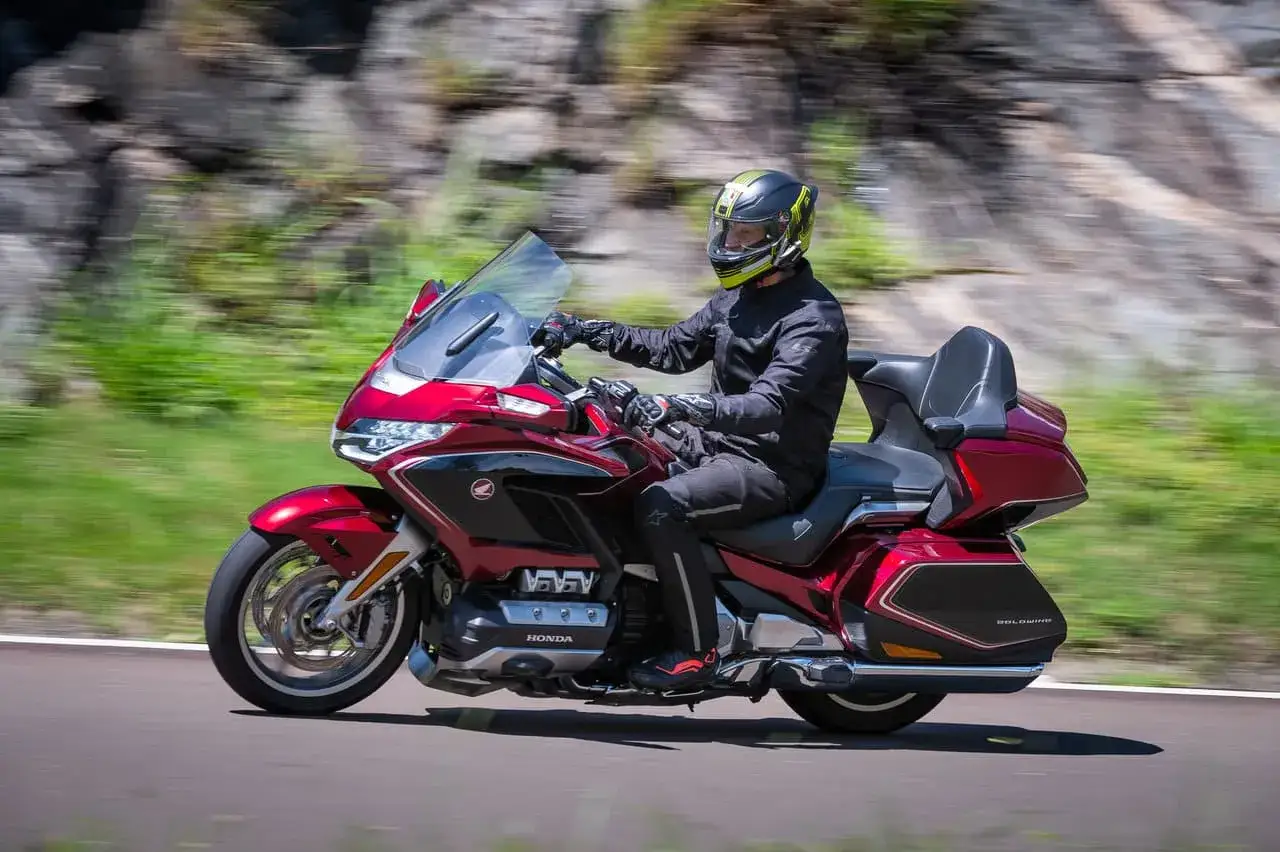 Mężczyzna w kasku jedzie czerwonym motocyklem Honda Gold Wing. To idealny, dobry motor szosowo turystyczny na długie trasy.