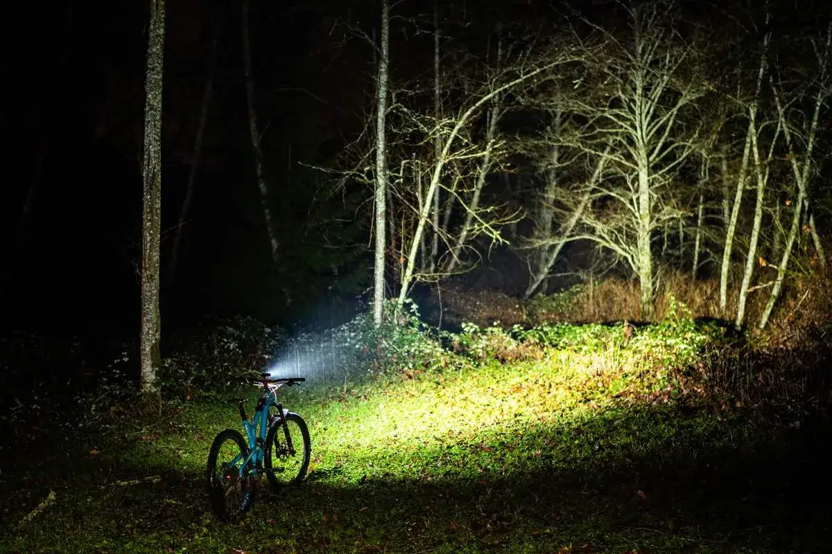 Rower elektryczny w lesie nocą, oświetlony mocnym światłem. Dowiedz się, jak włączyć światła w rowerze elektrycznym, by bezpiecznie jeździć po zmroku.