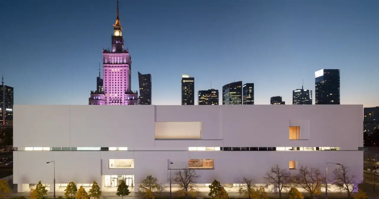 Nowe muzeum sztuki nowoczesnej w Warszawie, z Pałacem Kultury w tle, nocą.