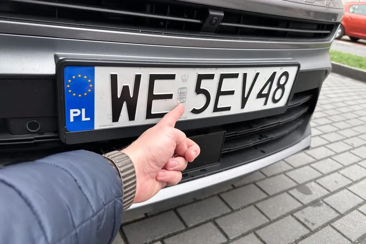 Palec wskazuje hologram na tablicy rejestracyjnej. Zastanawiasz się, ile trwa rejestracja samochodu przez internet?