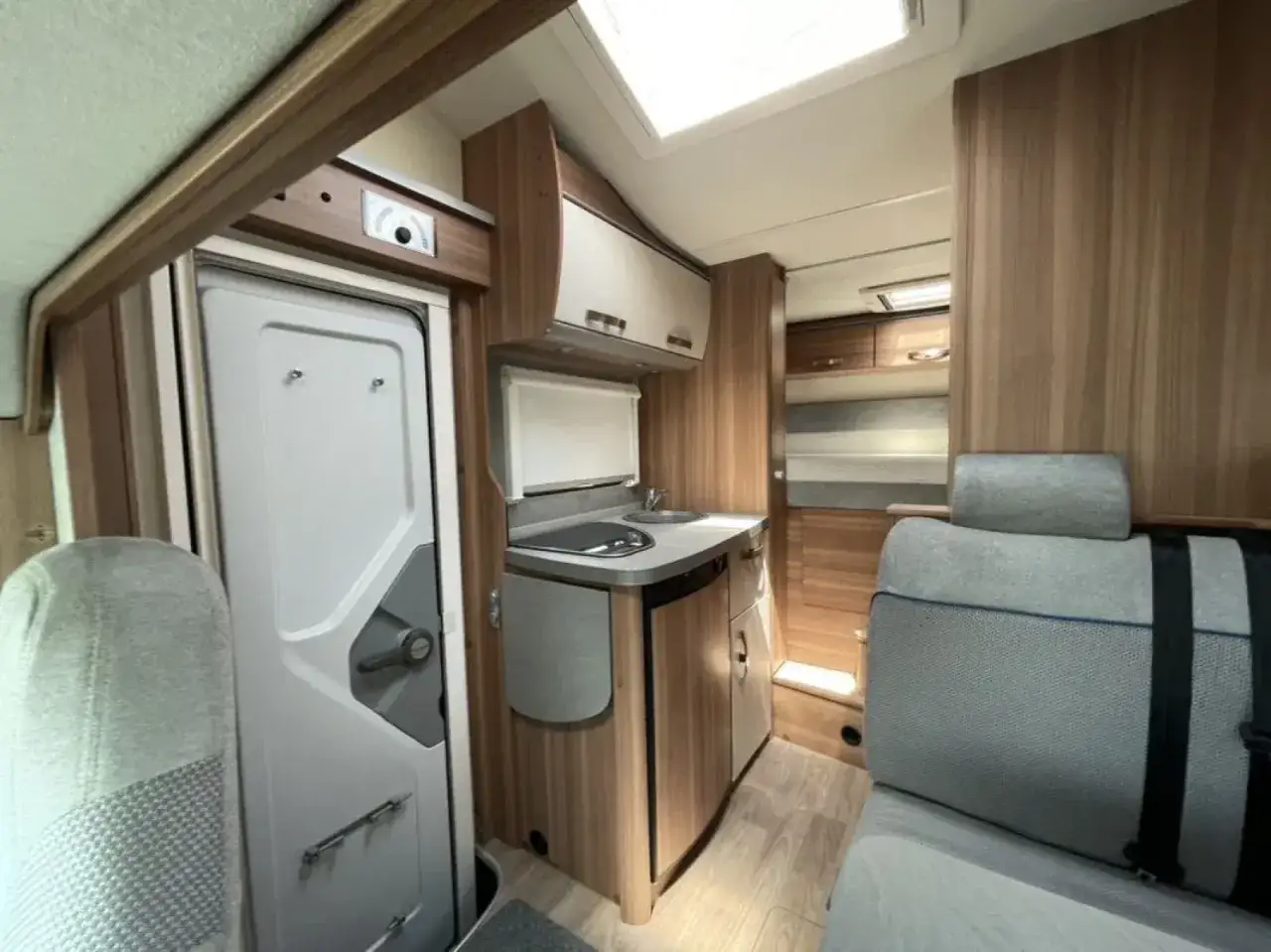 Wnętrze kampera alkowa: łazienka, aneks kuchenny z płytą grzewczą i zlewem, siedzenia.