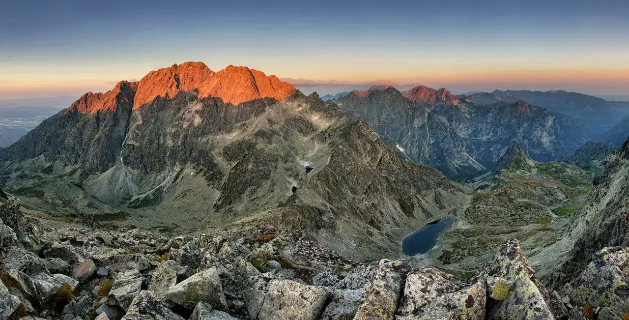Widok z trasy na Gerlach o wschodzie słońca. Skaliste zbocza, g&oacute;rskie jeziora i oświetlone szczyty Tatr Wysokich.