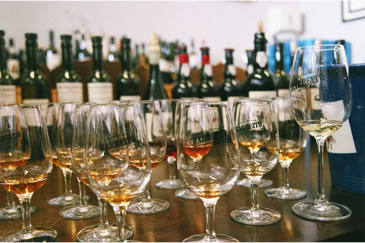 Szklanki z winem z Madery, gotowe do degustacji. W tle rzędy butelek tego szlachetnego trunku.