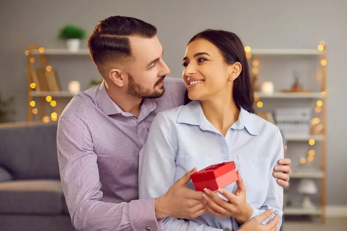 Szczęśliwa para wymienia spojrzenia, on wręcza jej prezent. Idealne kr&oacute;tkie cytaty o miłości szczęśliwej.