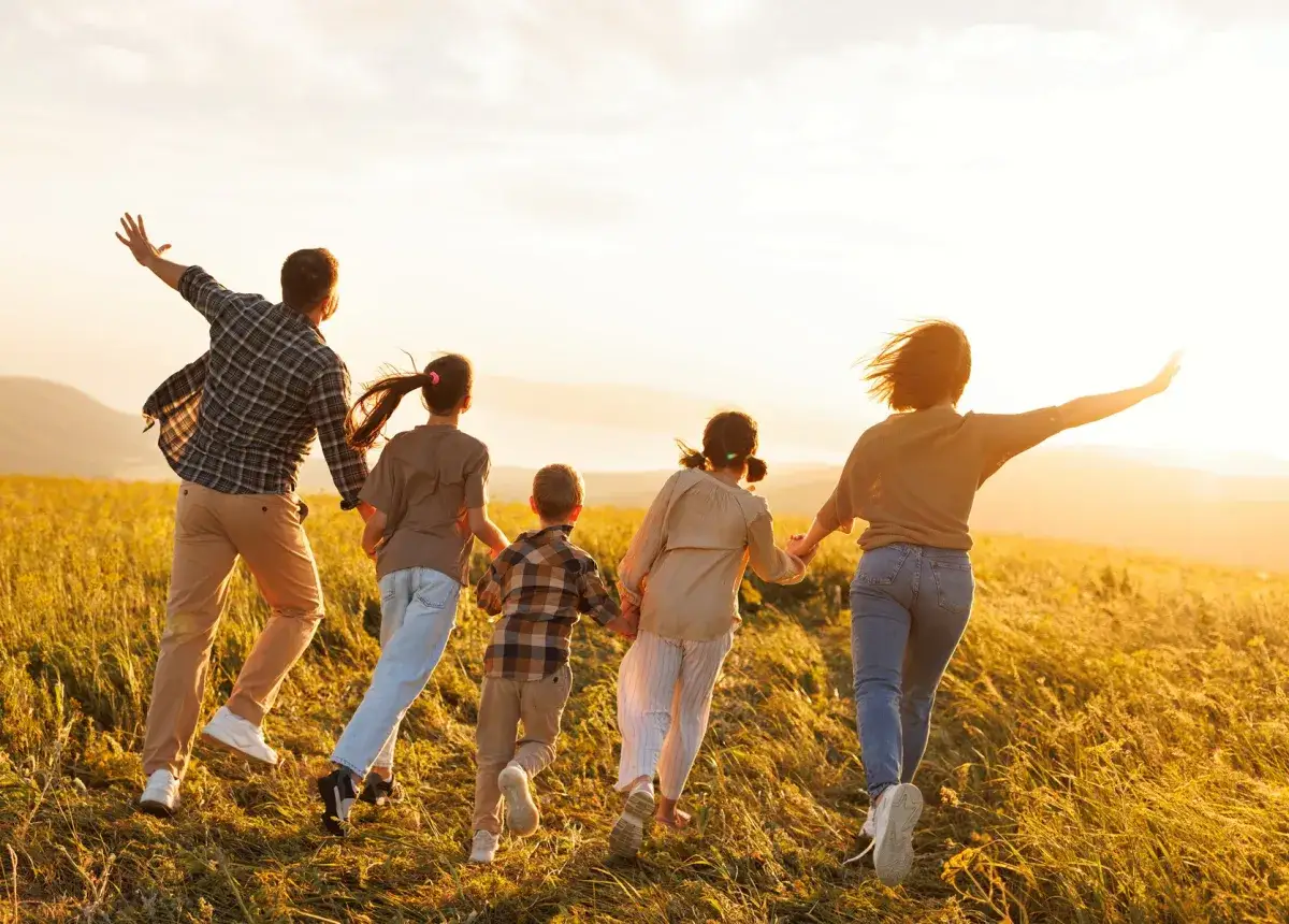 Rodzina biegnie przez pole o zachodzie słońca. Pokazuje, jak pogodzić pracę z opieką nad dzieckiem, czerpiąc radość z każdej chwili.