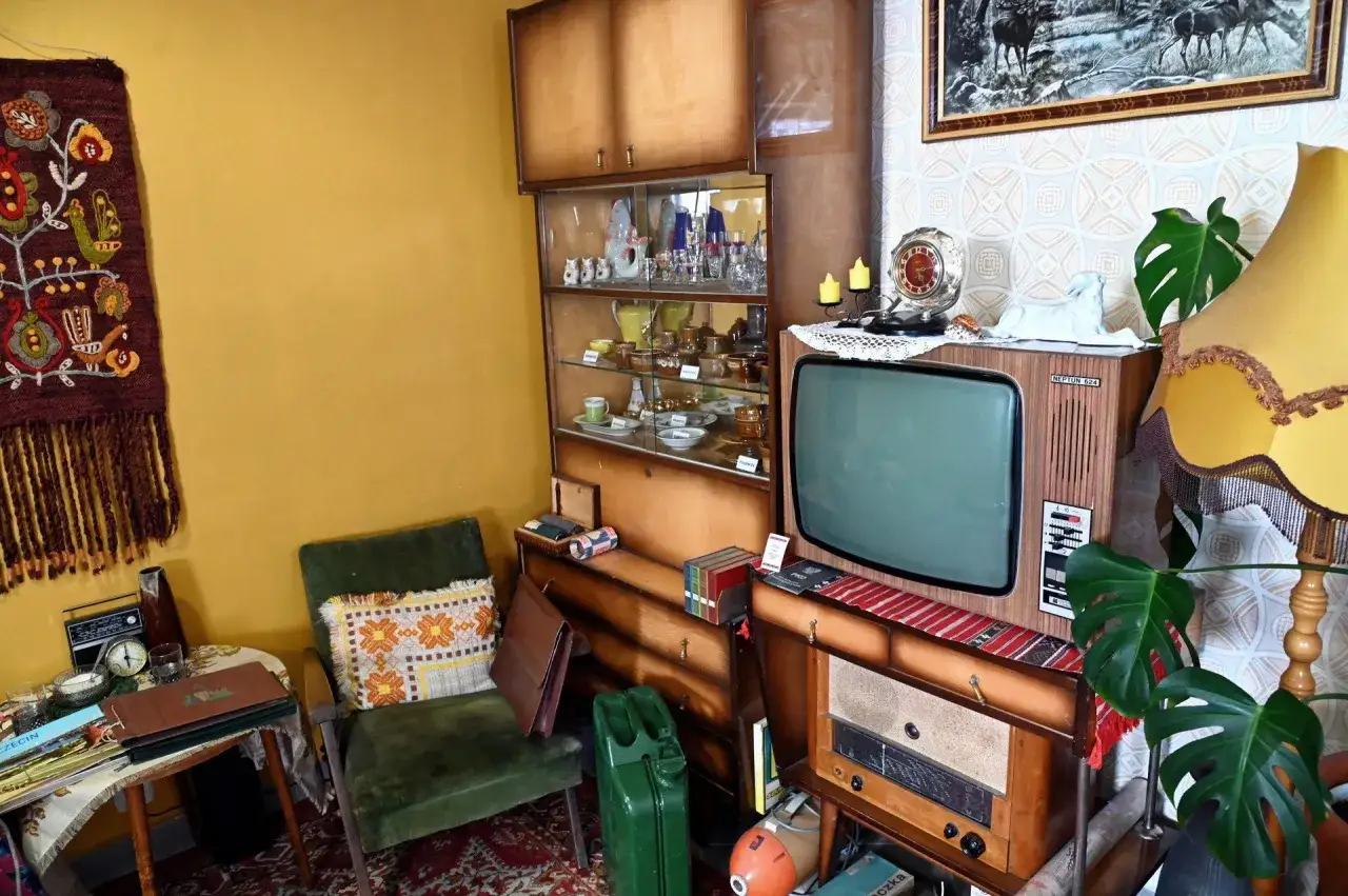 Wnętrze w stylu pok&oacute;j lata 80. z meblościanką, zielonym fotelem, starą telewizją i radiem.