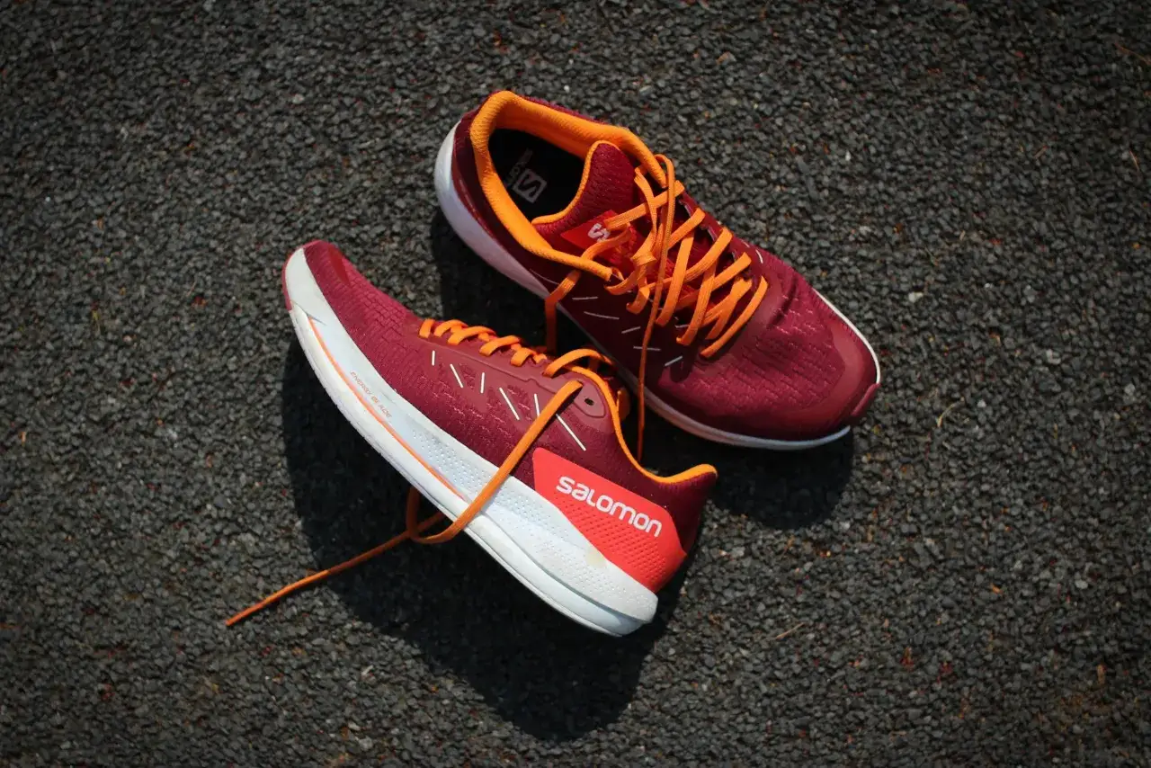 Biegowe buty Salomon w kolorze bordowym z pomarańczowymi sznur&oacute;wkami, idealne dla biegaczy z pronacją.