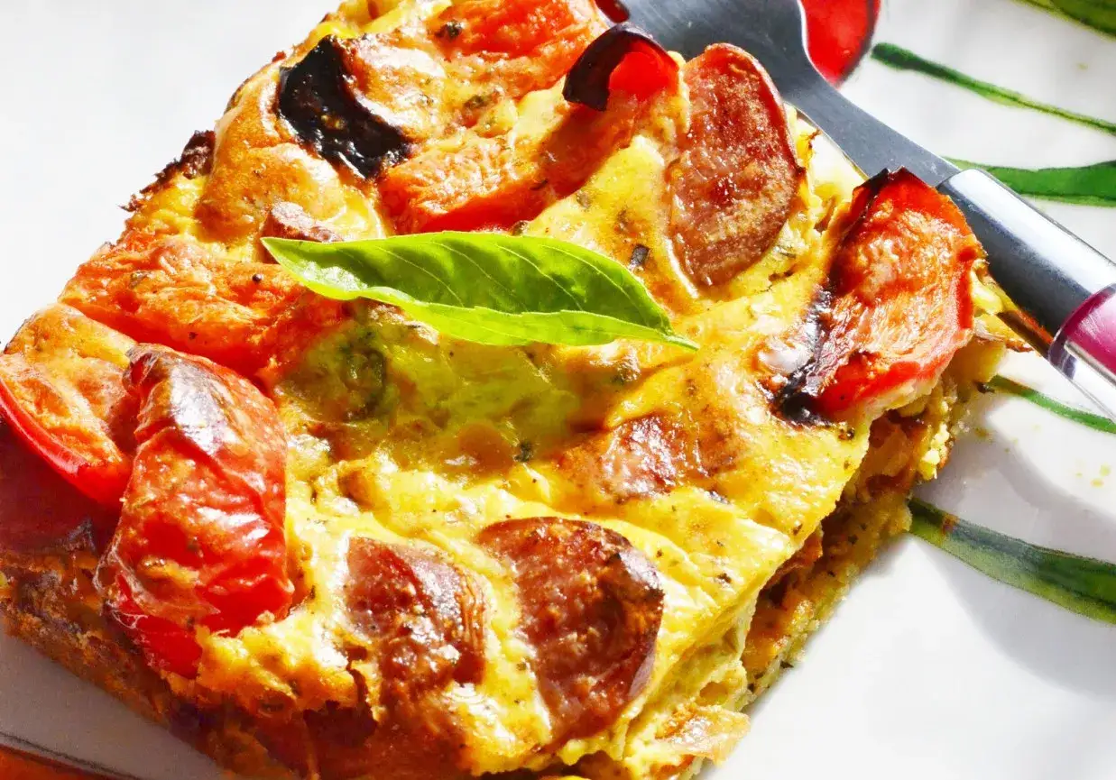 Pyszna tarta z kiełbasą, pomidorami i bazylią, podana na talerzu z zielonymi akcentami.