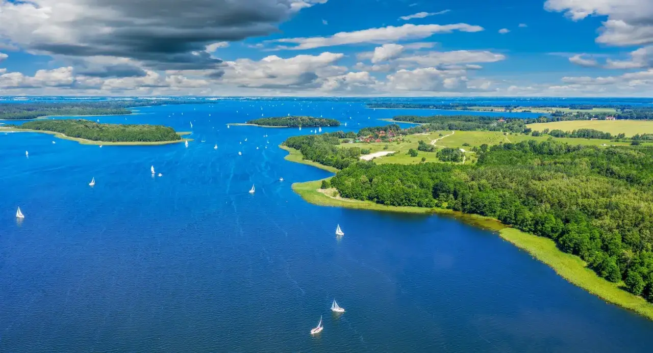 Mazury, gdzie na wakacje w Polsce? Jezioro pełne żagl&oacute;wek, zielone wyspy i błękitne niebo. Idealne miejsce na relaks i aktywny wypoczynek.