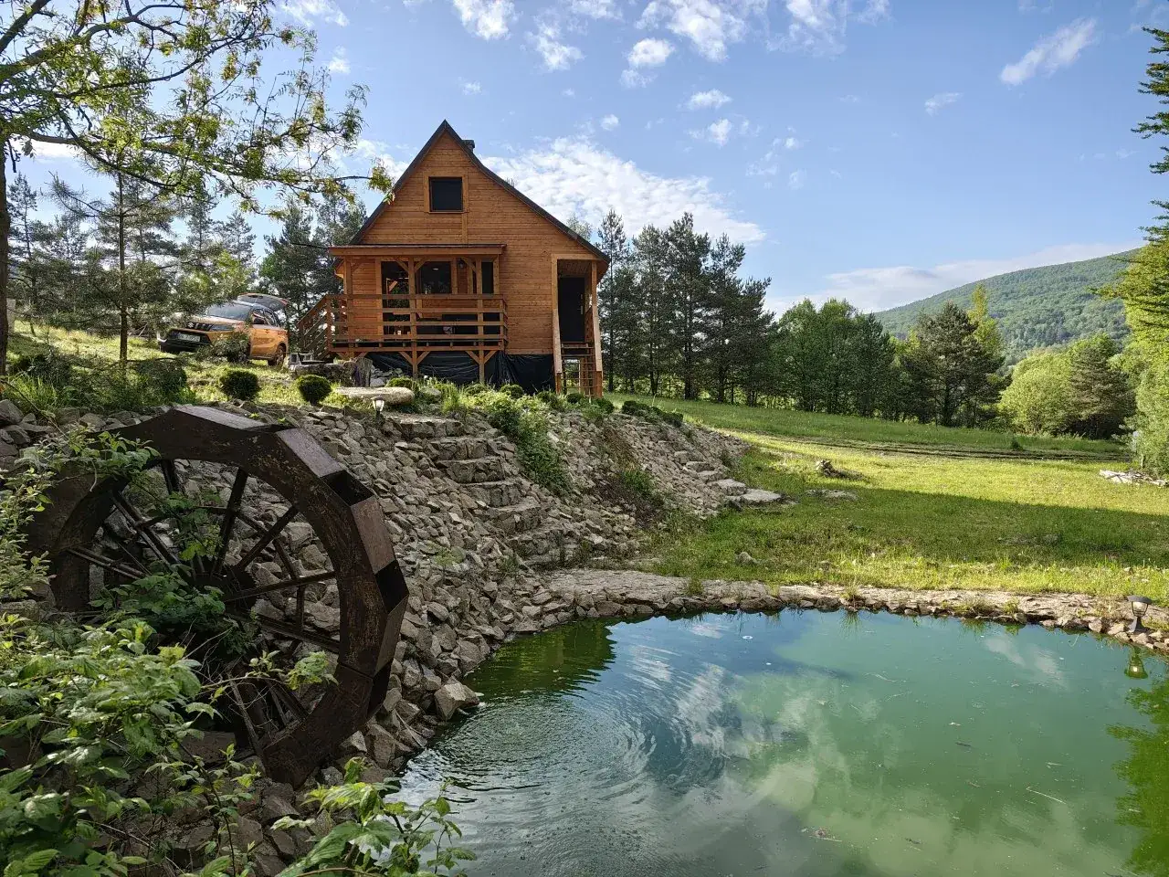 Drewniany domek z tarasem, staw z kołem wodnym i zielone wzgórza. Idealne miejsce, gdzie noclegi w Bieszczadach czekają na Ciebie.