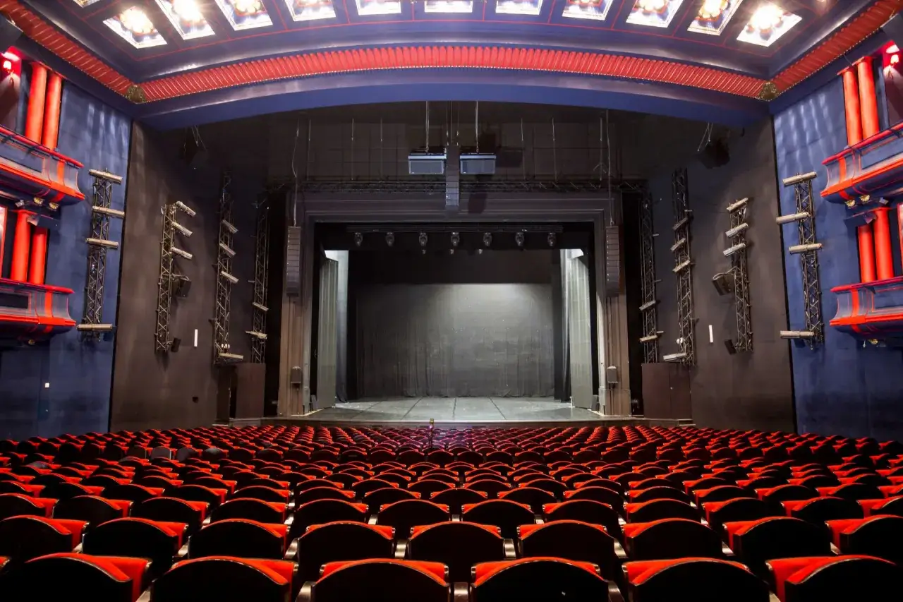 Pusta widownia Teatru Roma, z rzędami czerwonych foteli skierowanych ku scenie.