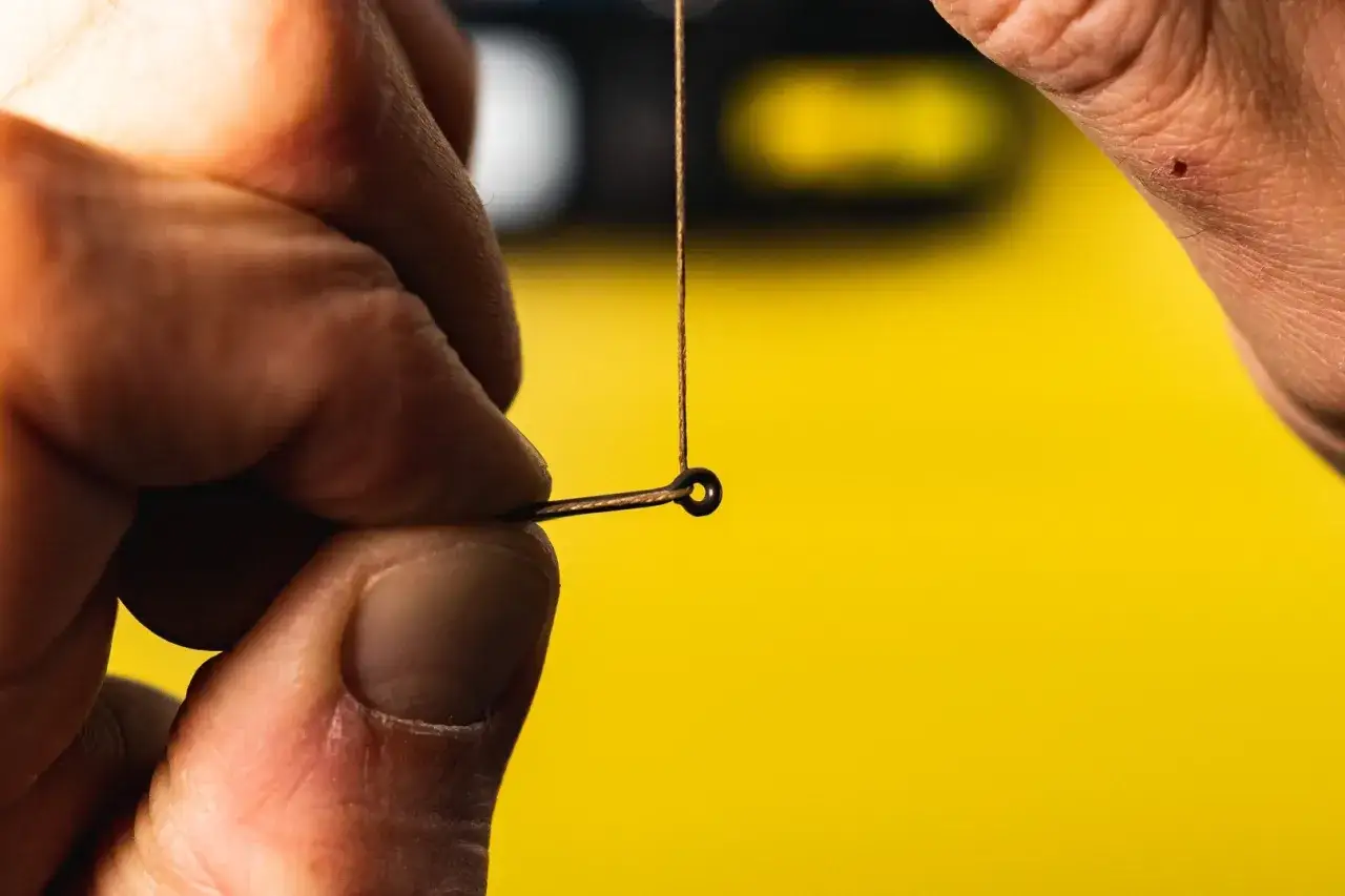 Dłonie przygotowują się, by pokazać, jak zawiązać haczyk z włosem. Precyzyjne ruchy palców nad cienką żyłką.