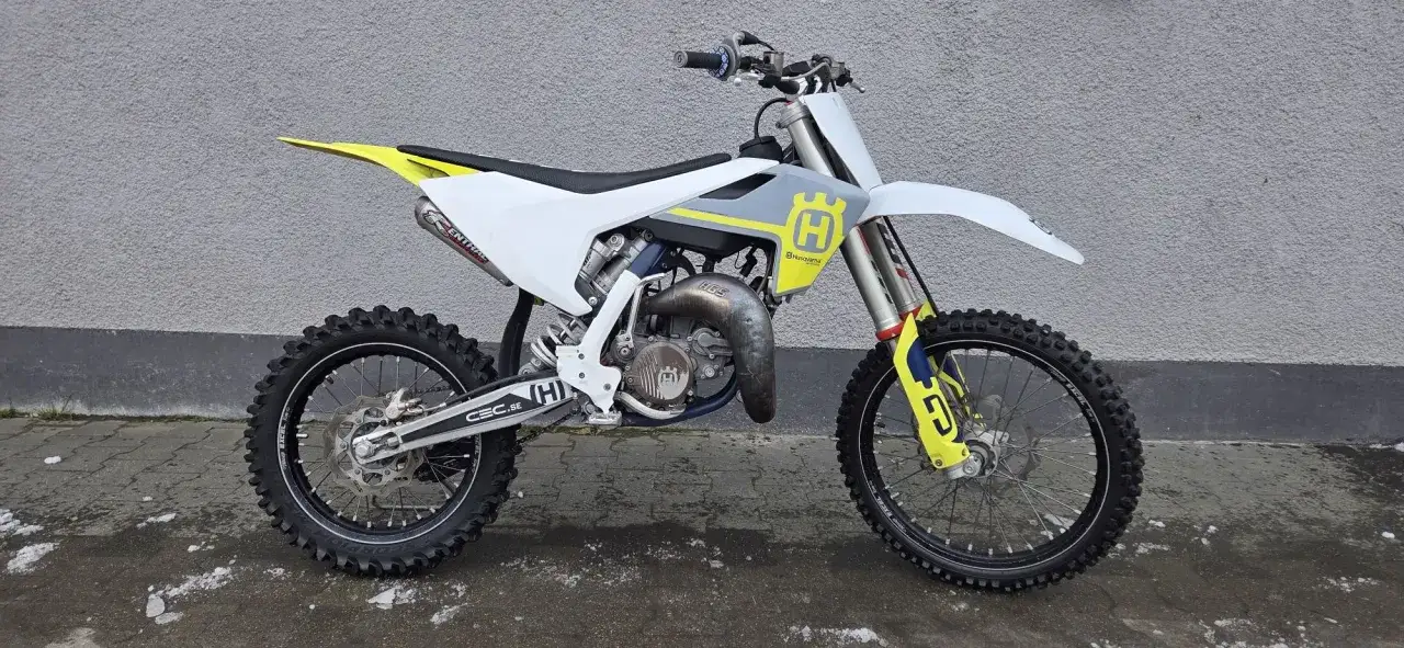 Husqvarna WRE 125 moc gotowa do akcji. Biało-szary motocykl crossowy z żółtymi akcentami, z dumą prezentuje swoją moc.