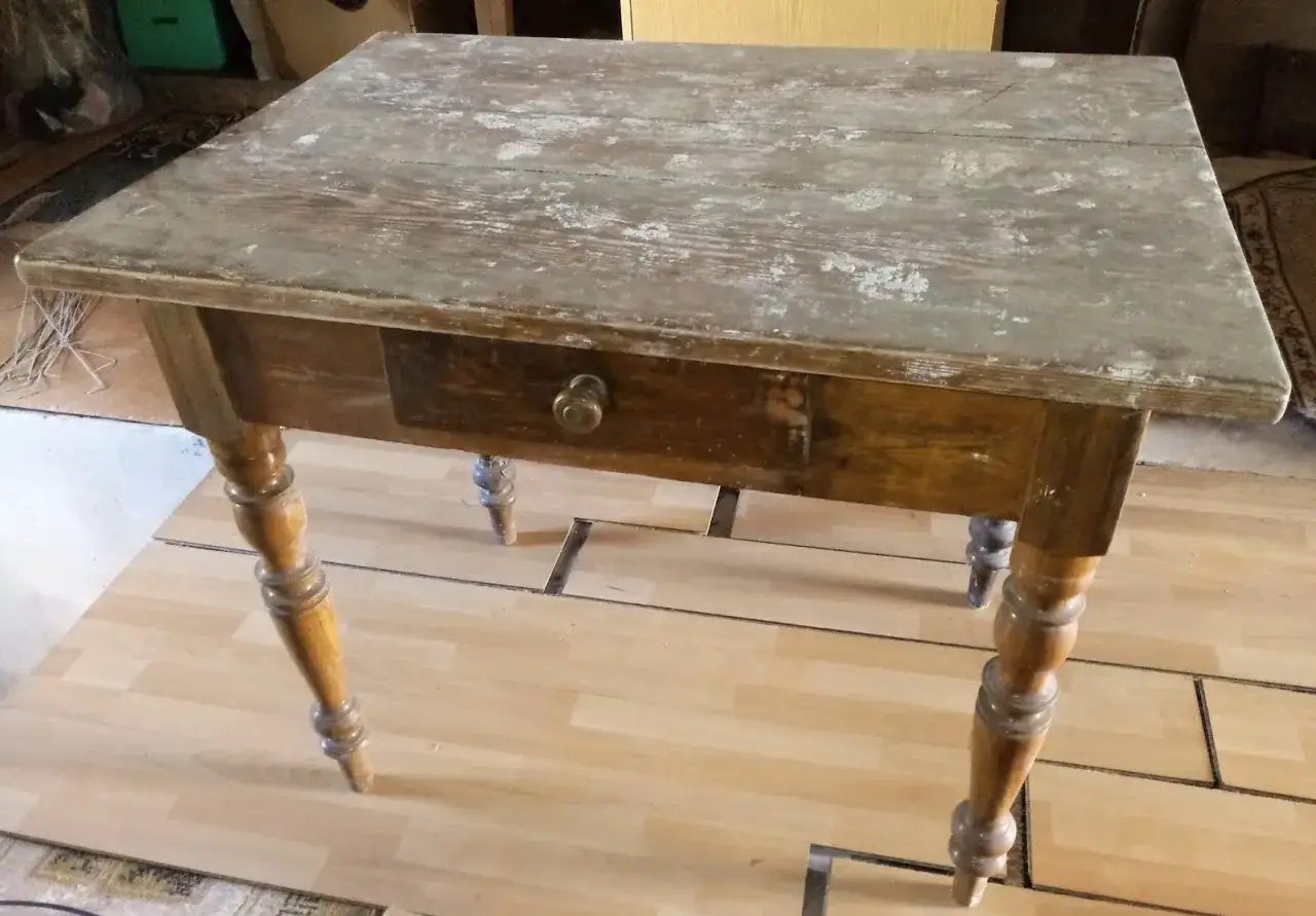 Stary drewniany stół z szufladą, gotowy do renowacji. Blat zniszczony, nogi ozdobne.