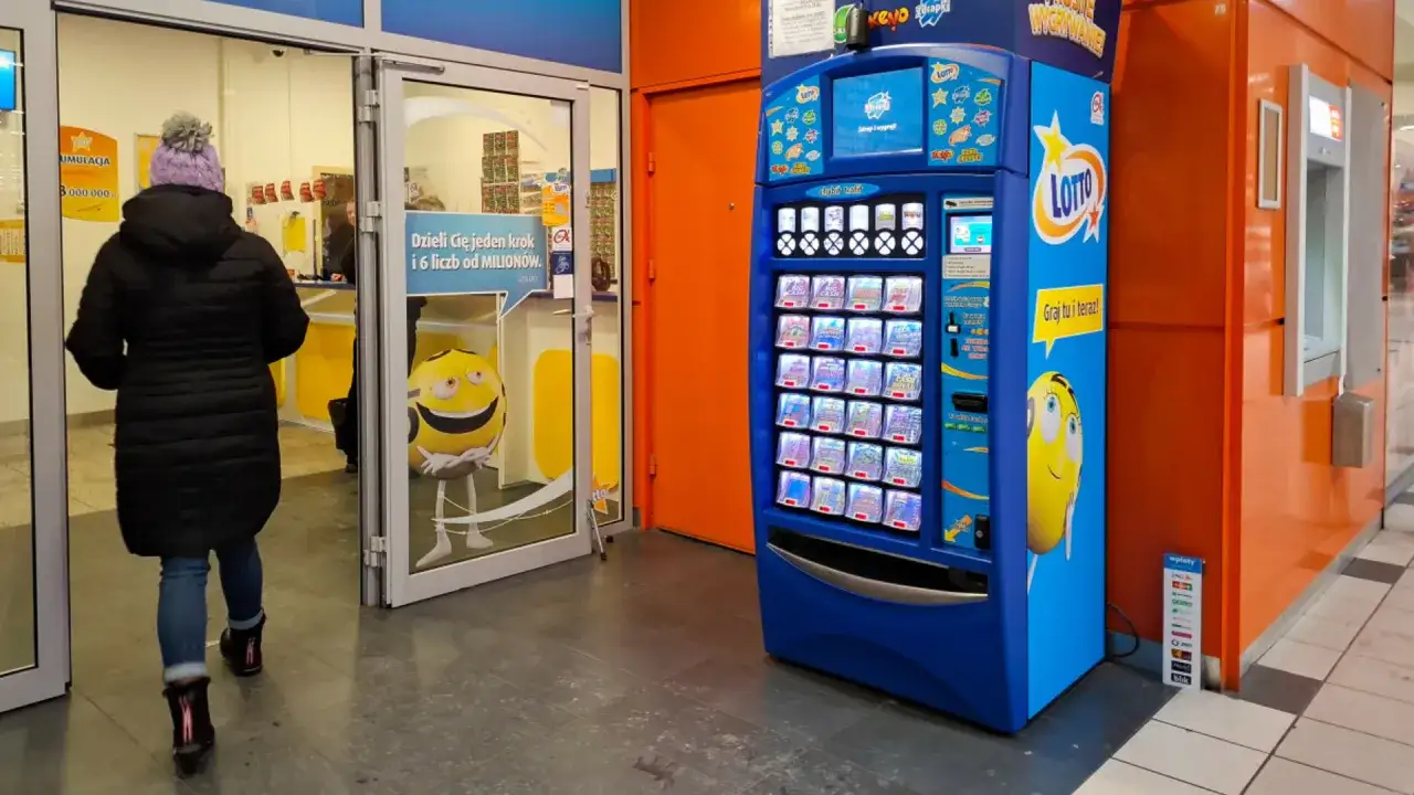 Kobieta wchodzi do punktu Lotto, gdzie może sprawdzić totolotka. Obok stoi automat z grami.