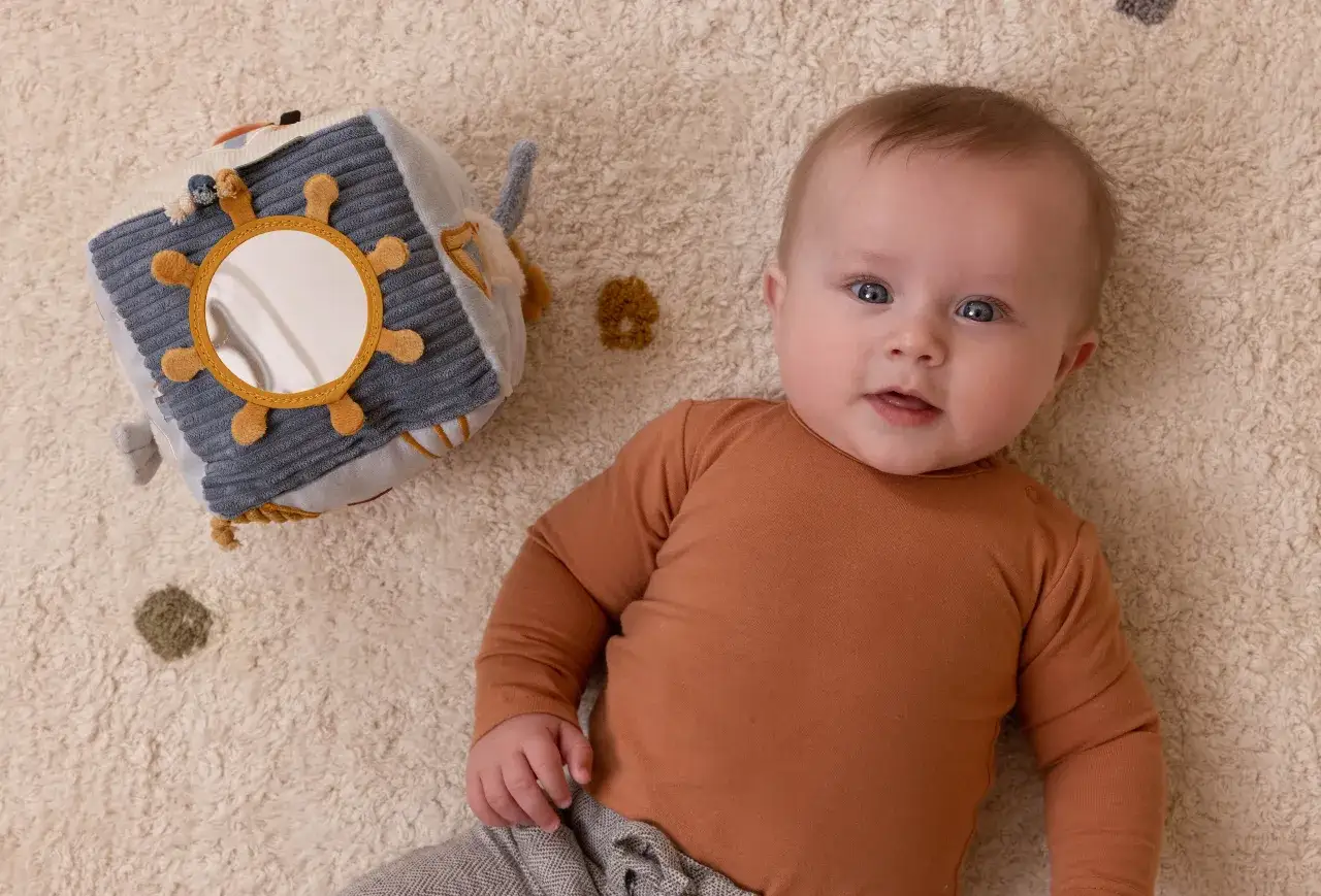 Uroczy niemowlak leży obok miękkiej kostki sensorycznej. Idealny pomysł na to, co kupić miesięcznemu dziecku, by rozwijać jego zmysły.