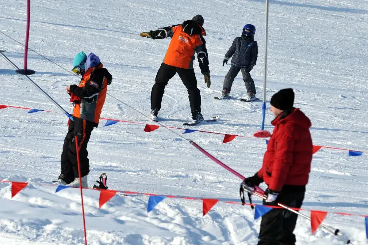 Narciarze na stoku, jeden z nich w pomarańczowej kurtce uczy dzieci. Zastanawiasz się, ile kosztuje kurs na instruktora narciarstwa?
