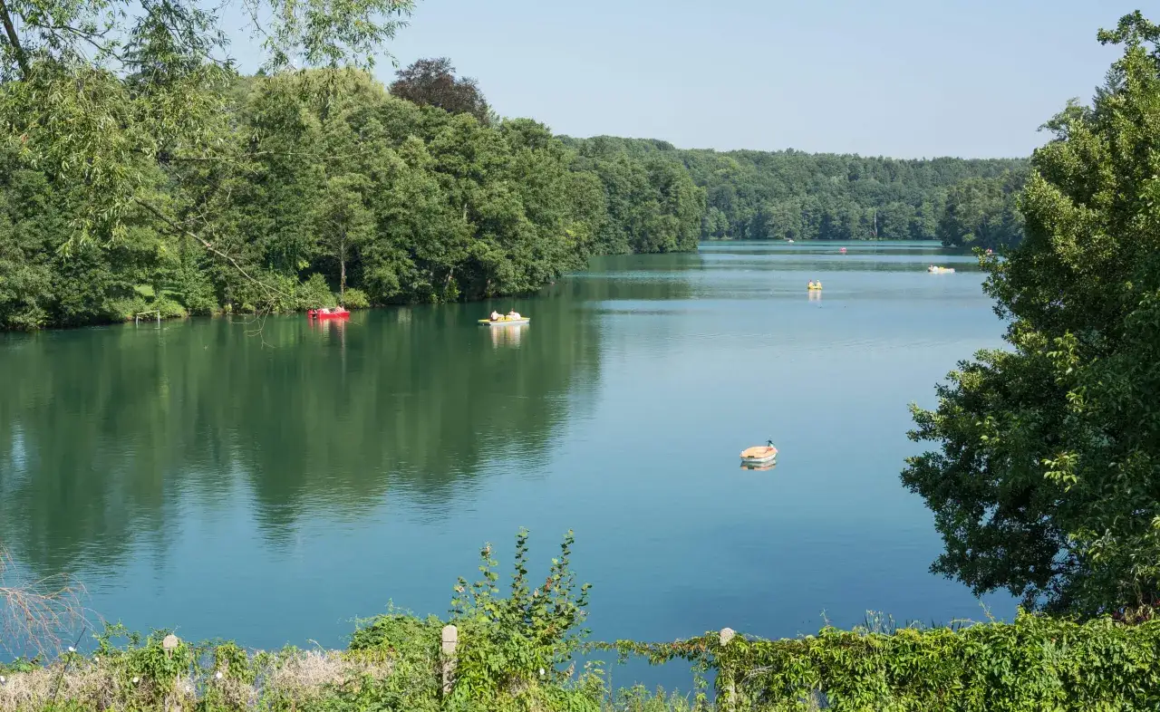 Spokojne jezioro Trześniowskie otoczone zielenią, z kilkoma łódkami na wodzie.