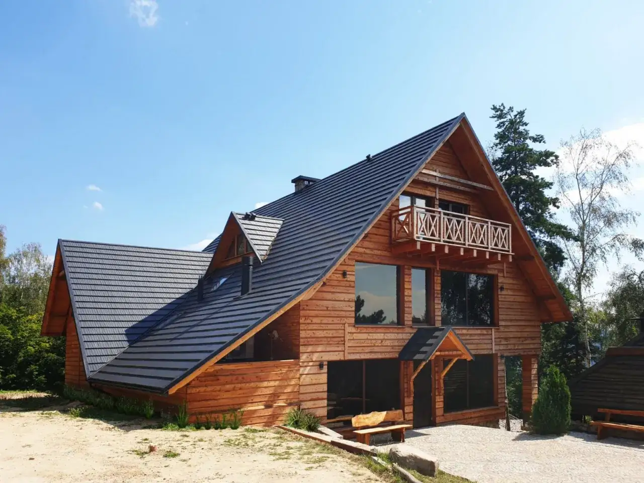 Drewniana bacówka na Jamnej z dużymi oknami i balkonem, otoczona zielenią.