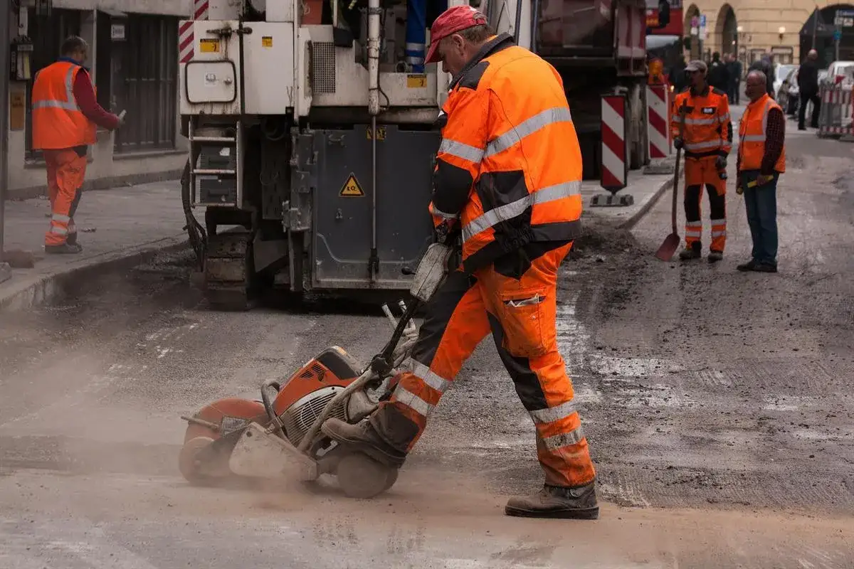 Robotnik w pomarańczowym stroju używa przecinarki do betonu. Wkładki przeciwhałasowe chronią jego słuch przed hałasem prac budowlanych.