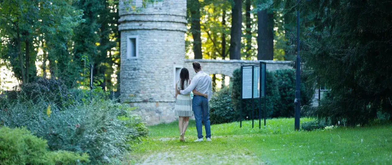 Para spaceruje po ogrodzie przy kamiennej wieży. Idealne miejsce na romantyczny pobyt w hotelu dla dorosłych Polska.