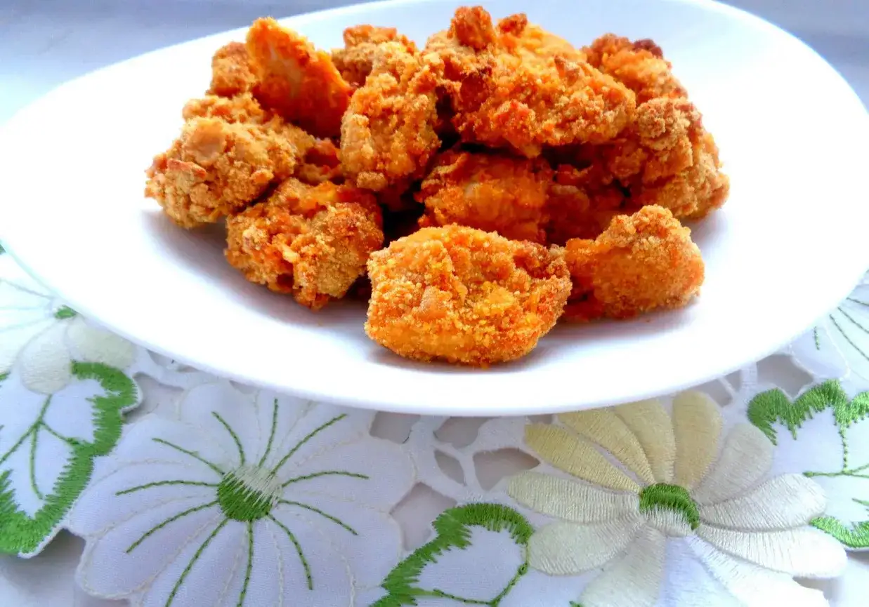 Chrupiące polędwiczki drobiowe kontra domowe nuggetsy. Pyszne kąski na białym talerzu, ozdobionym haftowanymi kwiatami.