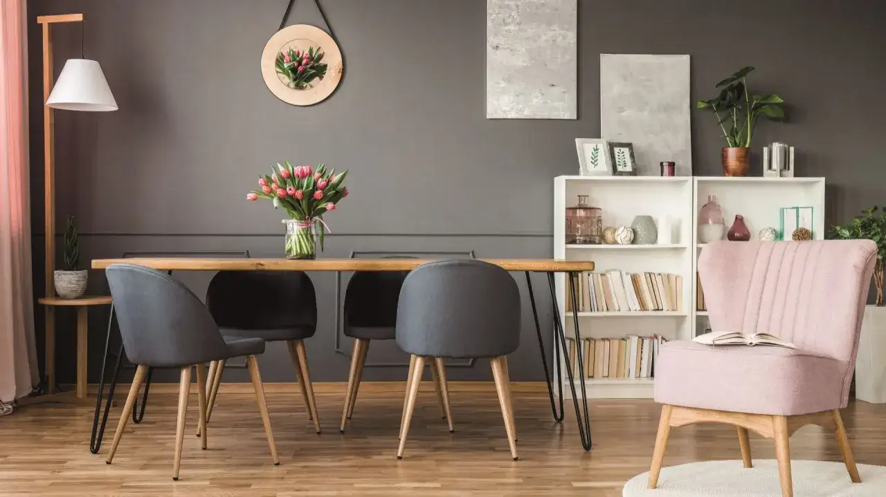 Szare ściany z czym łączyć? W tej jadalni szarość ścian świetnie komponuje się z drewnianym stołem, grafitowymi krzesłami i pastelowym fotelem.