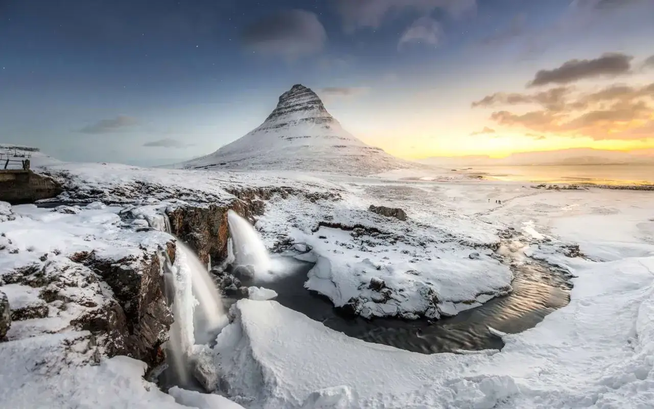Zimowy krajobraz Islandii, jak z Gry o Tron. G&oacute;ra Kirkjufell i wodospady w śnieżnej scenerii o zachodzie słońca.