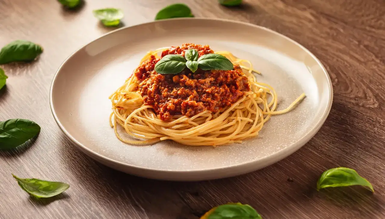 Pyszne spaghetti z sosem bolońskim, ozdobione bazylią. Idealne danie, gdy zastanawiasz się, jak podgrzać sos do spaghetti, by był aromatyczny.