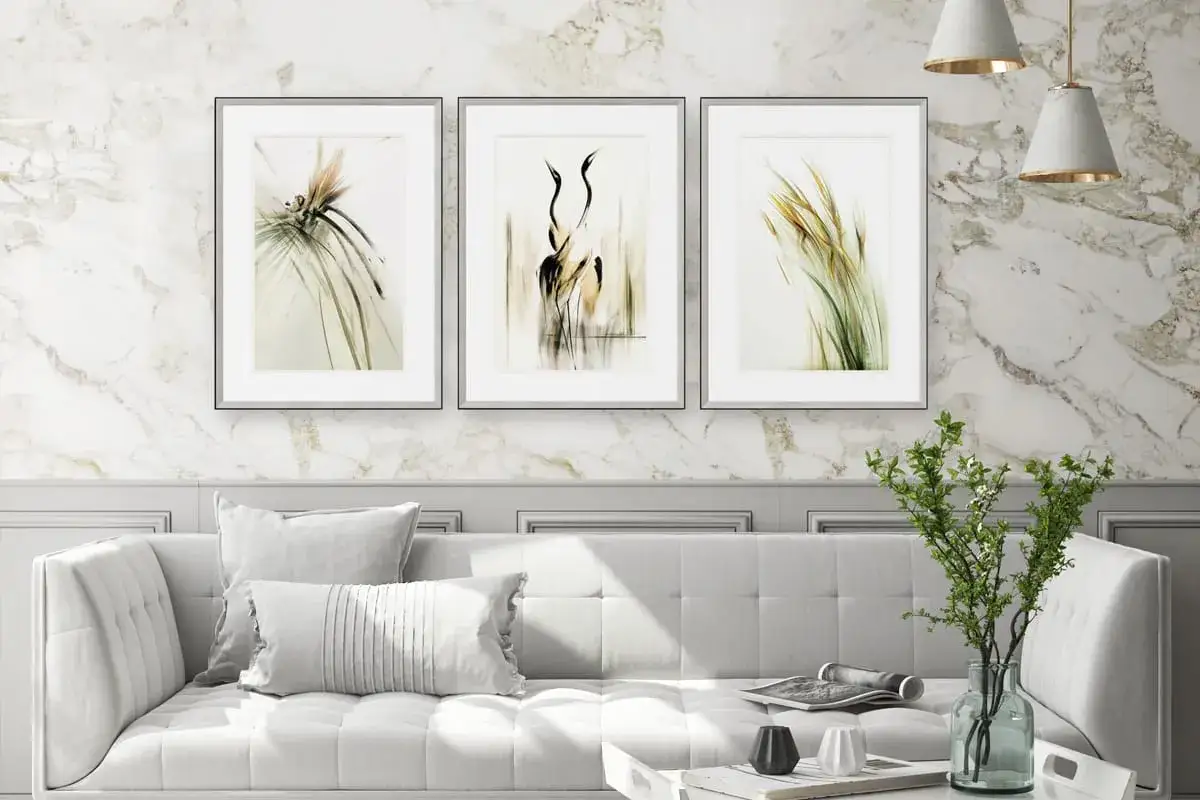 Eleganckie obrazy z ptakami i trawami nad białą sofą to świetny pomysł, jak udekorować ścianę.
