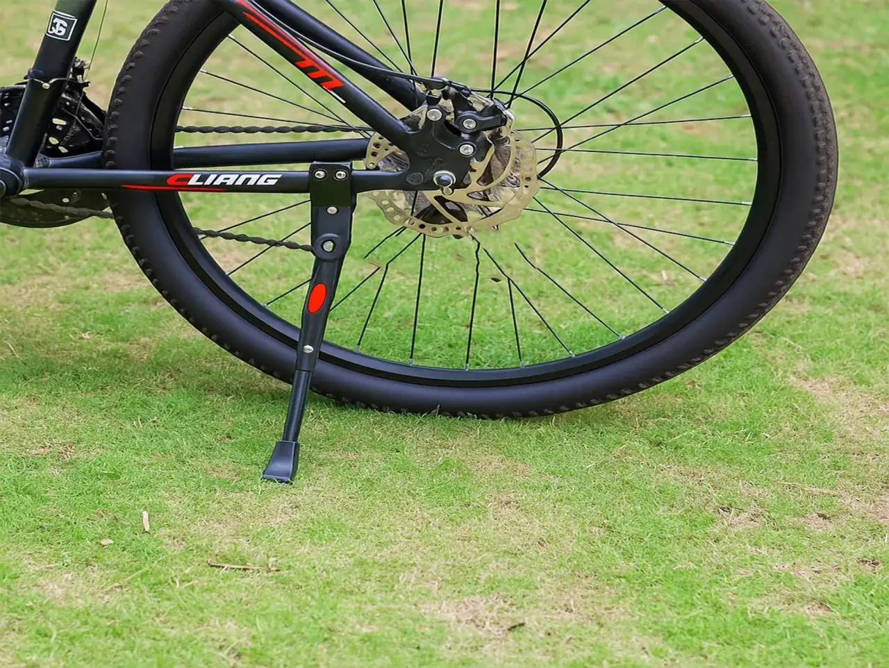 Montaż stopki rowerowej na tylnym kole roweru. Stopka jest czarna z czerwonym akcentem.