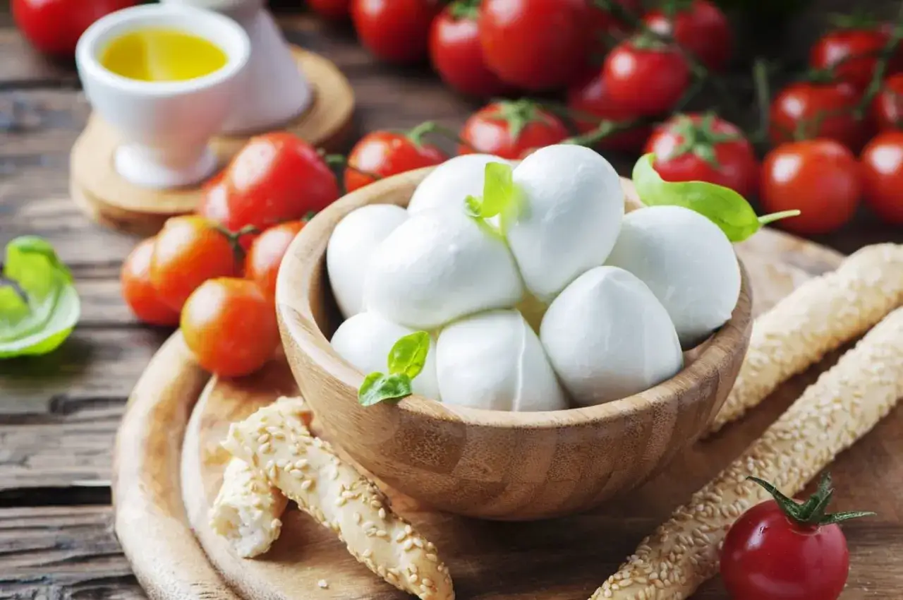 Kulki mozzarelli w drewnianej misce, pomidorki koktajlowe i oliwa. Czy mozzarella jest zdrowa? Tak, w umiarkowanych ilościach.