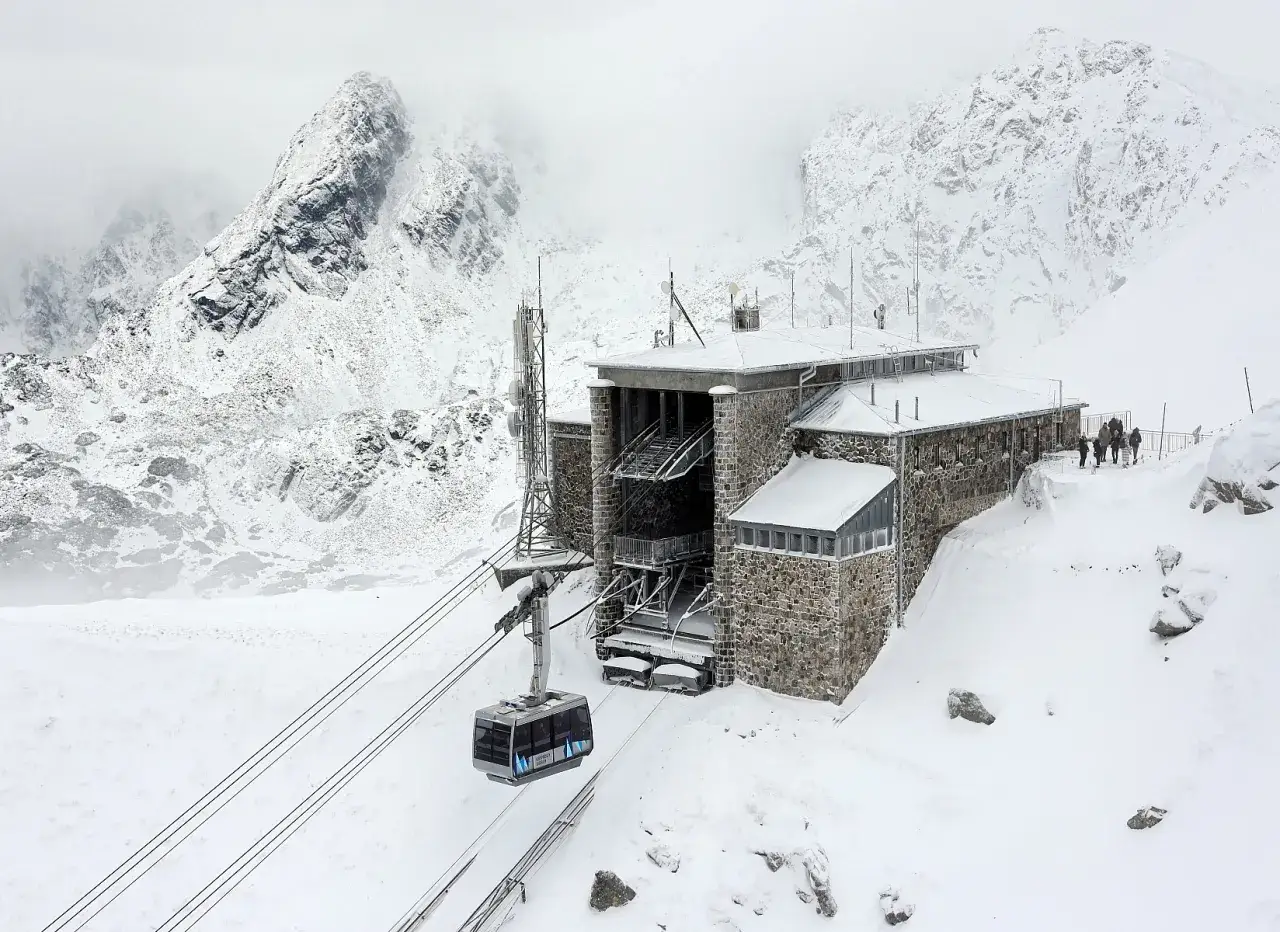 Kasprowy Wierch kolej w zimowej scenerii. Wagonik kolejki linowej zbliża się do kamiennego budynku stacji, otoczonego ośnieżonymi szczytami Tatr.