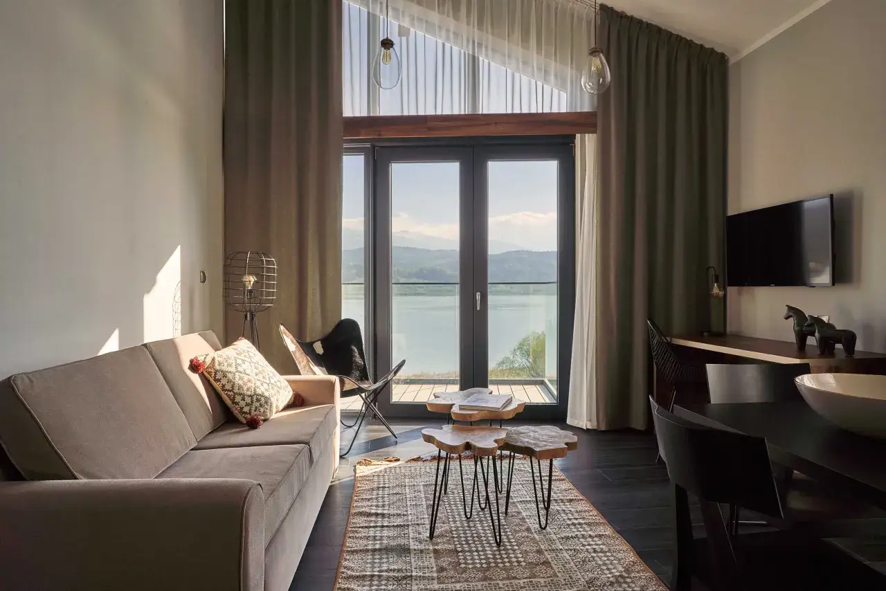 Przytulny pokój z widokiem na jezioro w hotelu Lake Hill Resort & Spa w Karkonoszach. Sofa, stoliki kawowe i krzesło motylkowe tworzą komfortową przestrzeń.