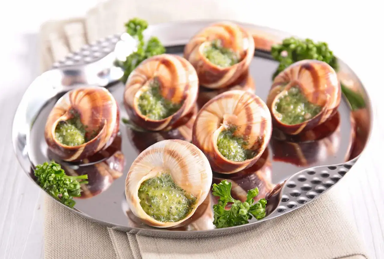 Ślimaki po burgundzku, czyli co jedzą Francuzi. Danie podane na metalowej tacy z natką pietruszki.