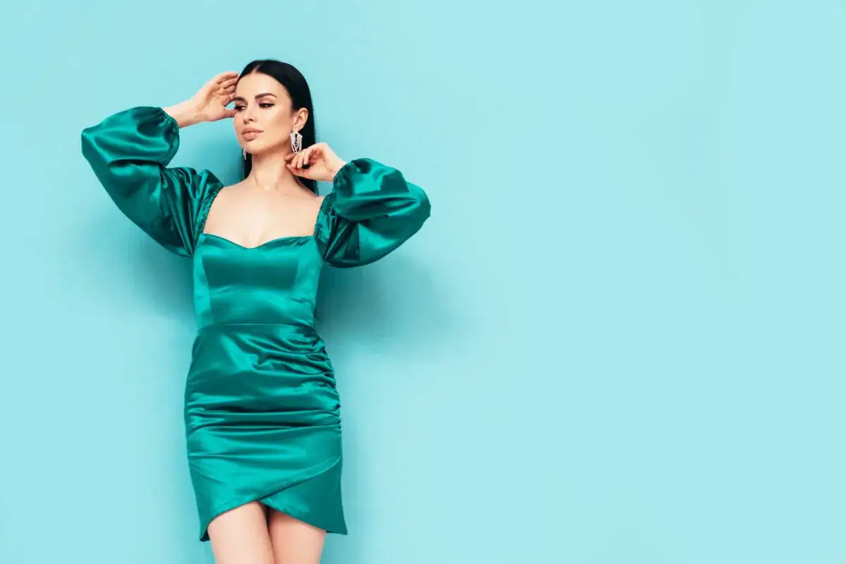 Elegancka kobieta w sukience w kolorze ciemny turkus z czym łączyć? Z błękitnym tłem i srebrnymi dodatkami.