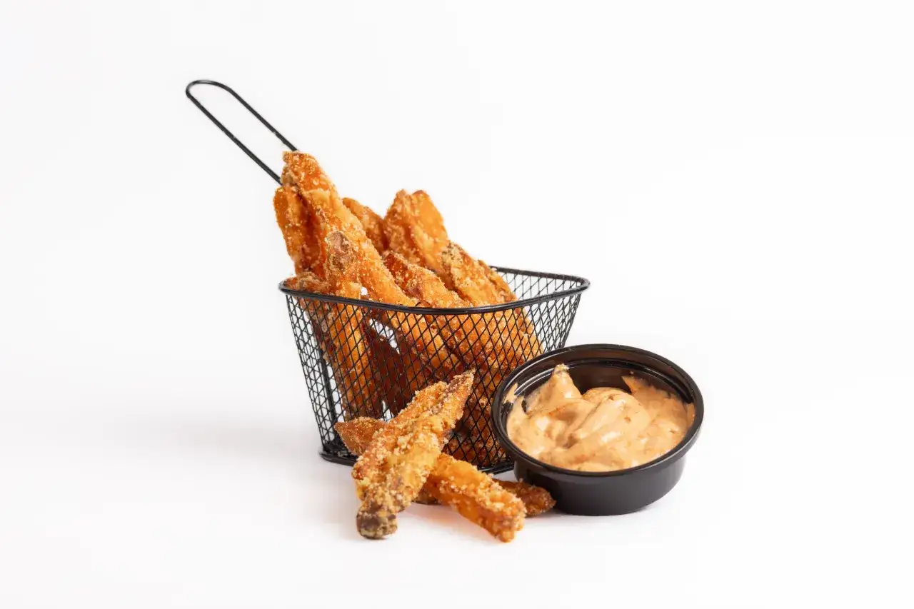 Chrupiące frytki z batatów w czarnym koszyczku, obok miseczka z kremowym sosem. Idealne co do frytek z batatów!