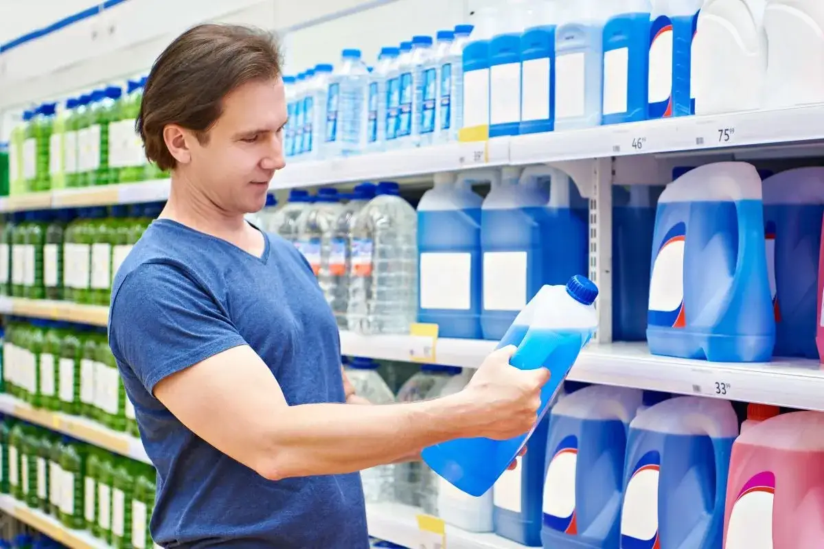 Mężczyzna w sklepie zastanawia się, czy można mieszać płyn chłodniczy, analizując niebieską butelkę.