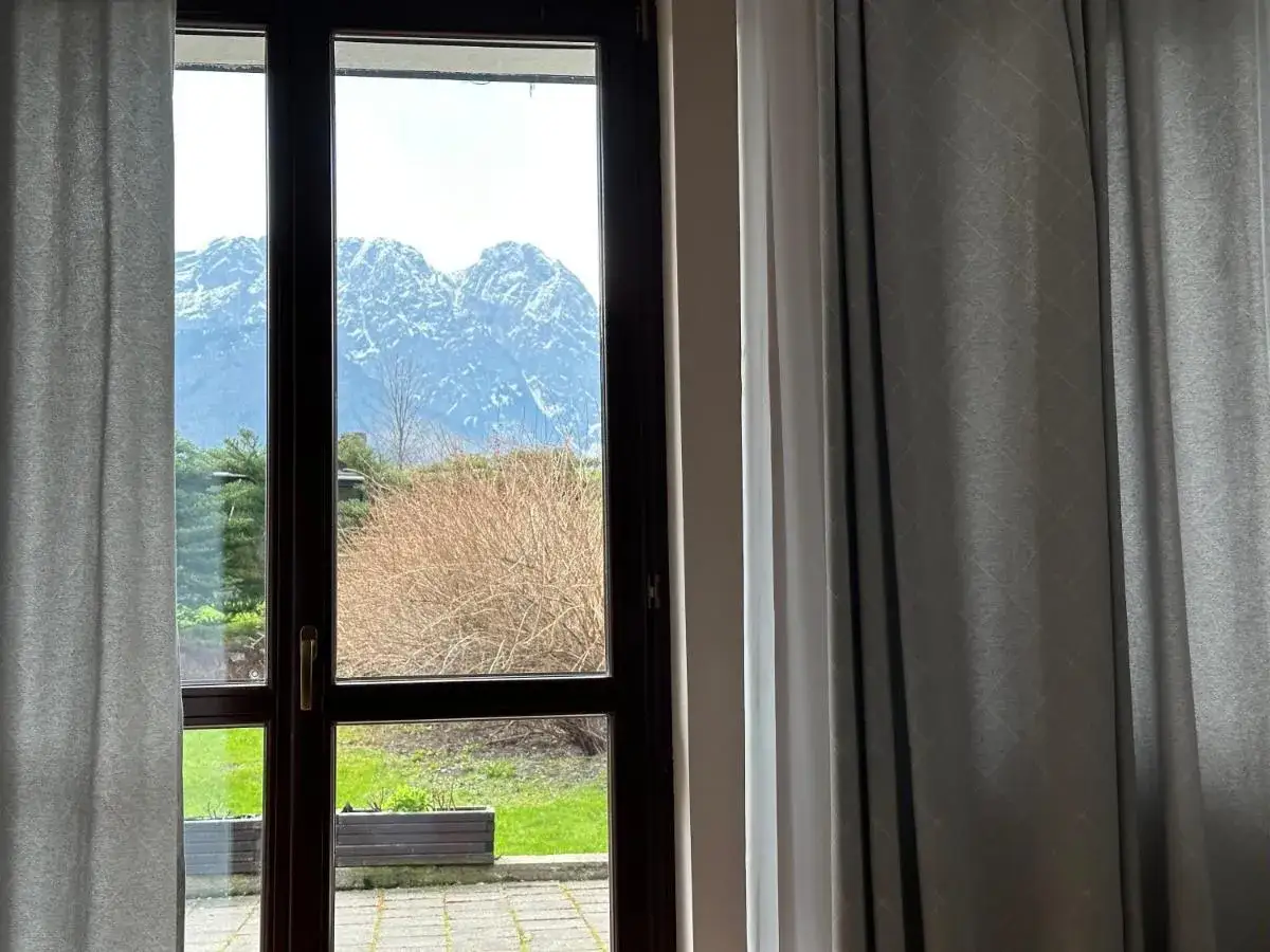 Widok z okna willi na wierchu w Zakopanem. Majestatyczne, ośnieżone szczyty Tatr g&oacute;rują nad zielonym ogrodem.