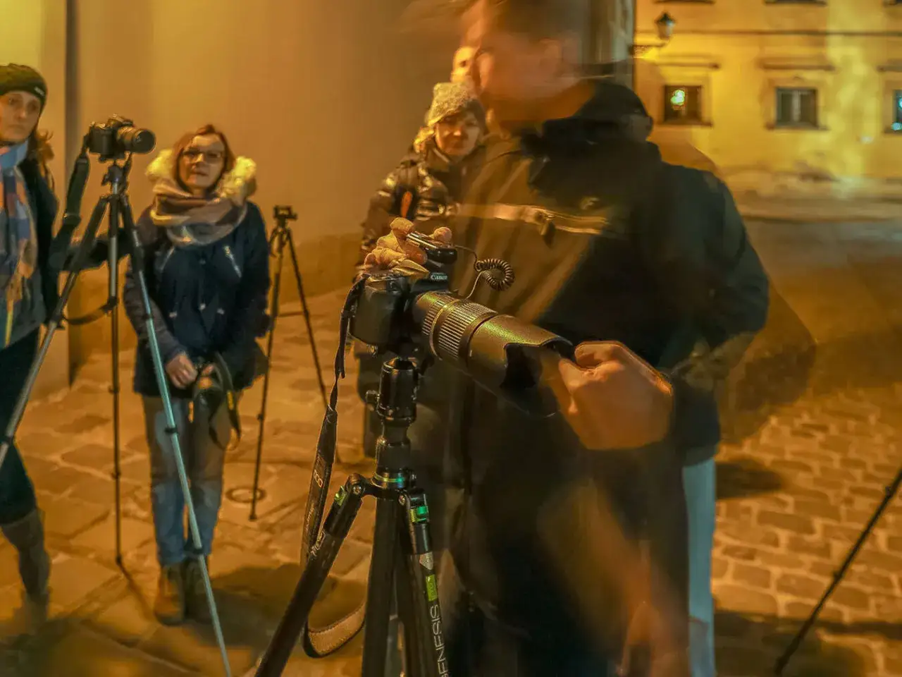 Uczestnicy kursu fotografii dla początkujących ćwiczą nocne fotografowanie. Widać kamery na statywach i ludzi w ciepłych ubraniach.