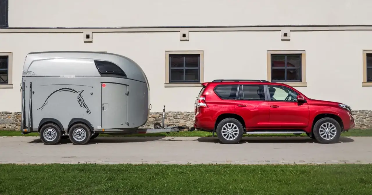 Czerwony SUV holuje przyczepę do przewozu koni kat B. Na przyczepie widnieje sylwetka konia.