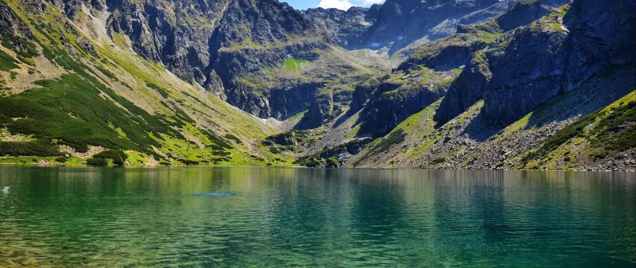 Zielony staw otoczony stromymi, skalistymi górami. Idealne miejsce, by zastanowić się, jakie szlaki warto zwiedzić w Zakopanem.